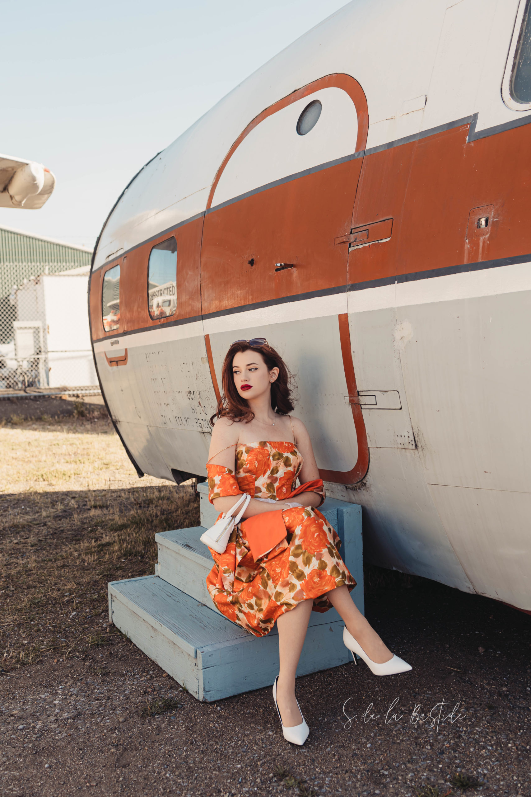 Retro themed Golden Age of Flight senior portrait.  Girl dress in vintage dress with bright orange flowers, taken at the Oakland Aviation Museum