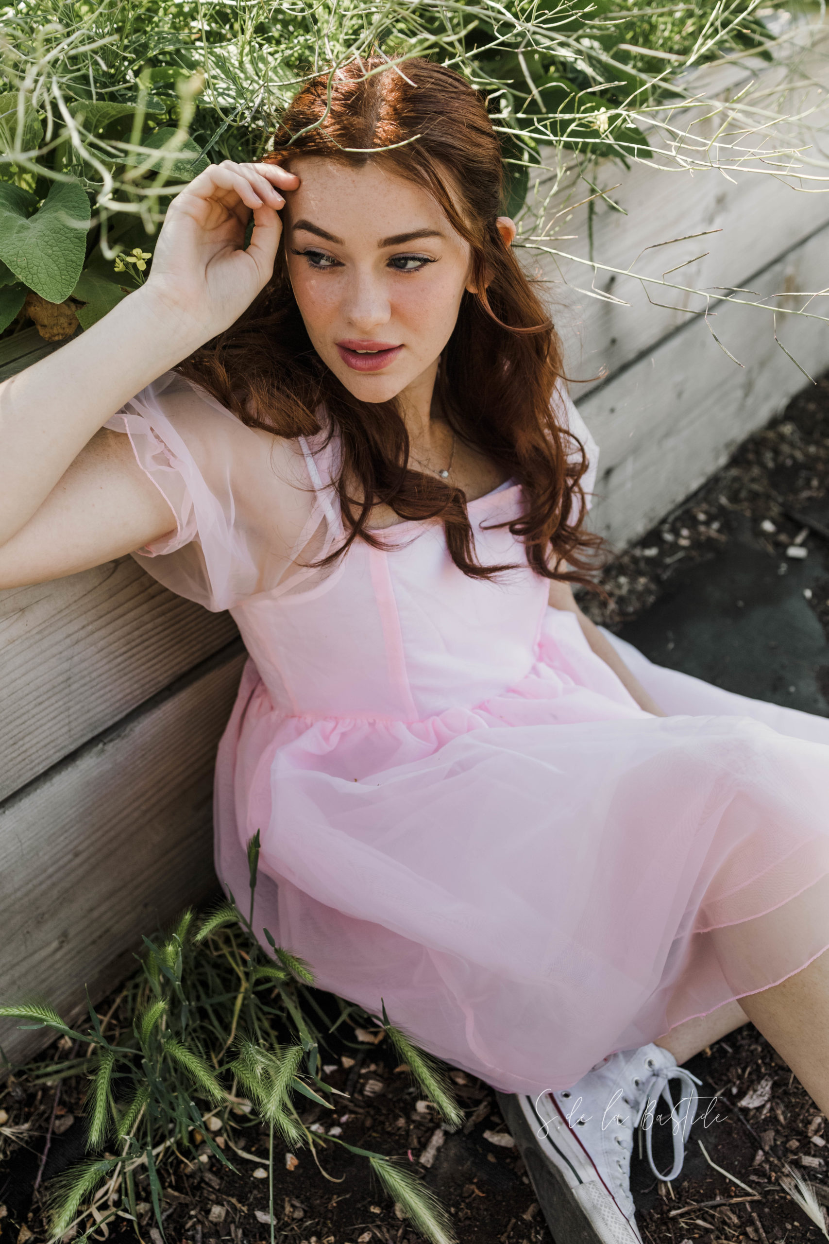 Bridgerton inspired Senior portraits taken in Vacaville at Soul Food Farm.  Girl with reddish hair, looking into the distance, dress in a baby pink poofy dress.